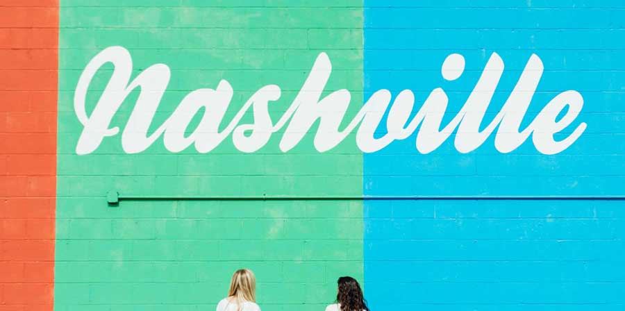 Two young ladies looking up at a mural with the word Nashville paint in white script.